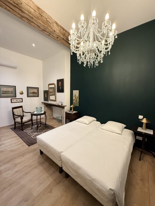Chambre élégante au gîte Le Montreal à Montréal du Gers avec lustre en cristal, mur d'accent vert et literie blanche