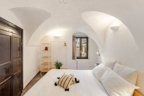 Chambre moderne avec plafond blanc voûté à l'appartement Talking Stones à Dolceacqua, lit, étagères en bois et vue ville