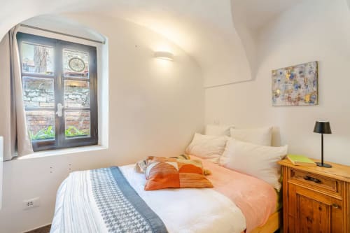 Chambre cosy de l'appartement Talking Stones à Dolceacqua avec vue sur la ville, mobilier en bois et accents orange chaleureux