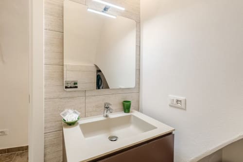 Salle de bain moderne au Talking Stones BnB à Dolceacqua avec lavabo blanc, miroir éclairé et finitions en carrelage bois