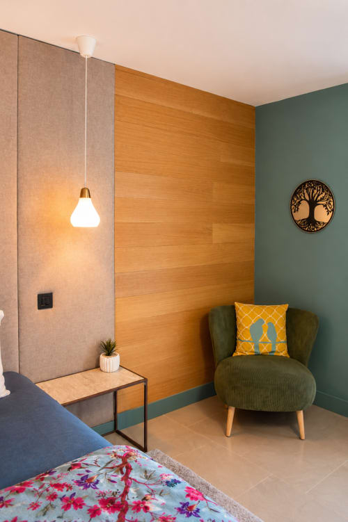 Chambre Cédrat à Au Pied Des Oliviers : chambre moderne avec fauteuil vert, panneaux muraux en bois et luminaires suspendus