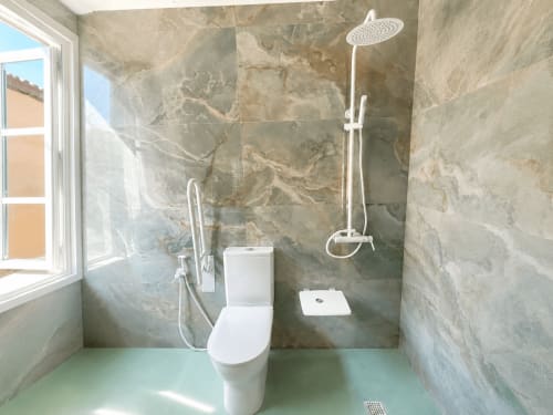 Baño moderno y accesible en apartamento Holibai, Baiona, con ducha de lluvia, inodoro blanco y paredes con azulejos de mármol