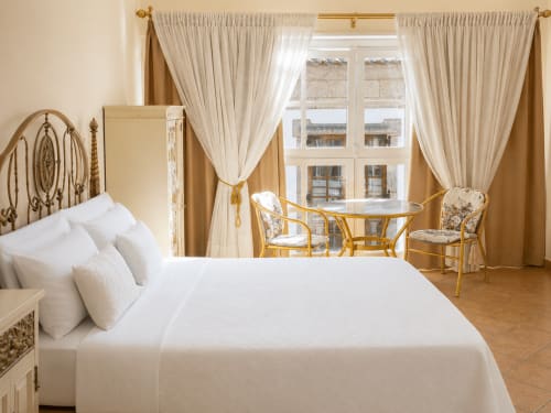 Elegante dormitorio en apartamento de Baiona con cama blanca, detalles dorados, vistas a la ciudad y zona de descanso