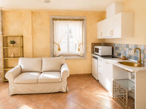 Luminoso estudio en Baiona con sofá crema, cocina americana y ventana con vista a la ciudad