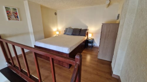 Chambre lumineuse avec lit en bois, tables de nuit, lampes, parquet et balustrade—vue sur mer à Saint-Cyr-sur-Mer