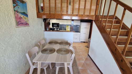Table à manger blanche avec sets de table tressés et chaises dans la cuisine d'un appartement à Saint-Cyr-sur-Mer, avec escalier en bois