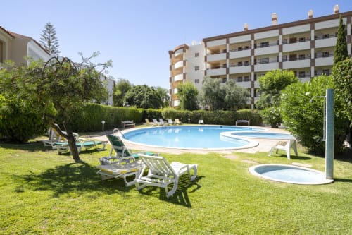 Área de piscina do RB Algarve com espreguiçadeiras, piscina azul e edifícios residenciais em Vilamoura, Portugal