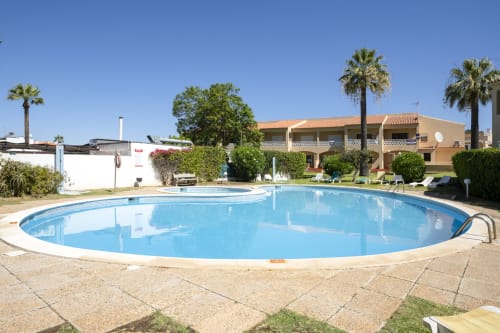 Grande piscina oval do hotel RB Algarve em Vilamoura, Portugal, com palmeiras e edifício bege ao fundo