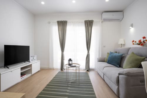 Moderna sala de estar do apartamento RB Algarve Vilamoura com sofá cinzento, TV inteligente, tapete às riscas e portas de vidro com acesso à piscina