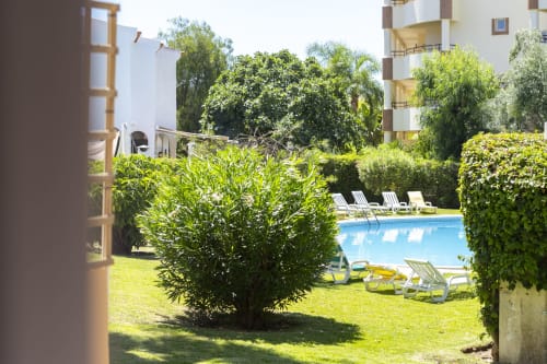 Vista da piscina do hotel RB Algarve com espreguiçadeiras, jardins exuberantes e edifício de apartamentos em Vilamoura, Portugal