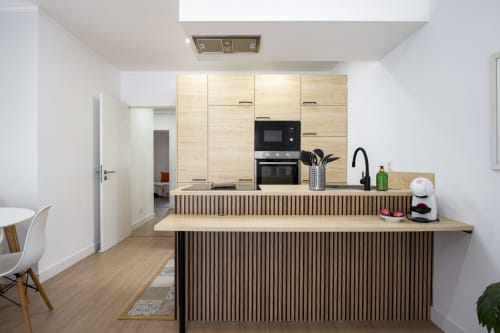 Cozinha moderna do apartamento RB Algarve com armários em madeira clara, eletrodomésticos pretos e bancada de café da manhã com banquetas