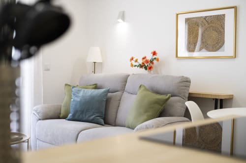 Sala moderna em apartamento RB Algarve com sofá cinzento, almofadas coloridas, flores laranja e arte geométrica na parede