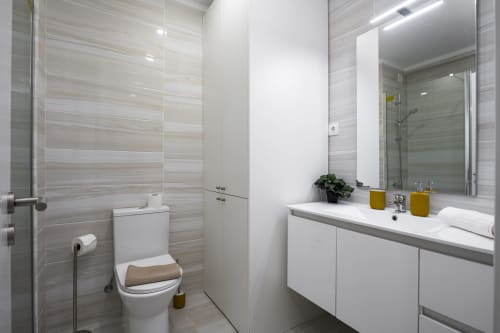 Banheiro moderno do apartamento RB Algarve com cuba branca, azulejos listrados, espelho e box de chuveiro em Vilamoura.