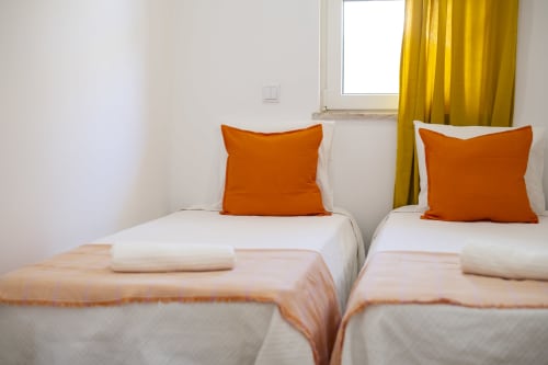 Camas de solteiro com almofadas laranja e mantas pêssego no apartamento-hotel RB Algarve em Vilamoura, Portugal
