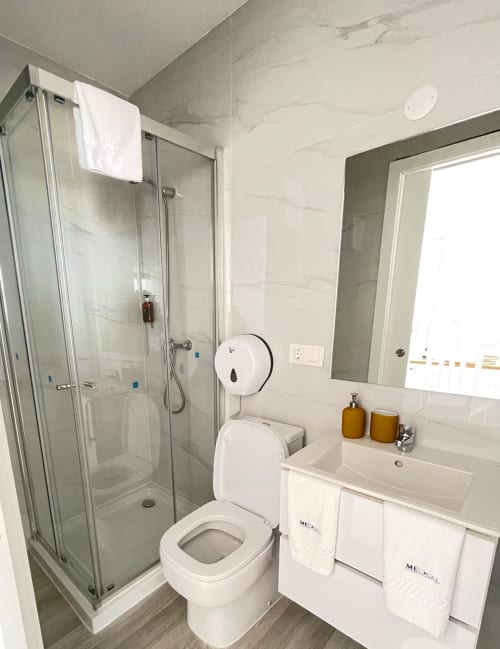 Banheiro moderno no apartamento MedSal Residence, Santa Maria. Chuveiro em vidro, vaso sanitário branco, pia com espelho e comodidades