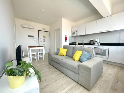 Apartamento estúdio moderno na MedSal Residence em Santa Maria com sofá cinza, cozinha branca, área de refeições e vista da cidade