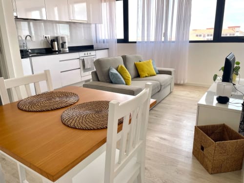 Apartamento T1 moderno na MedSal Residence em Santa Maria com sala integrada, cozinha branca, sofá cinzento, mesa de jantar e