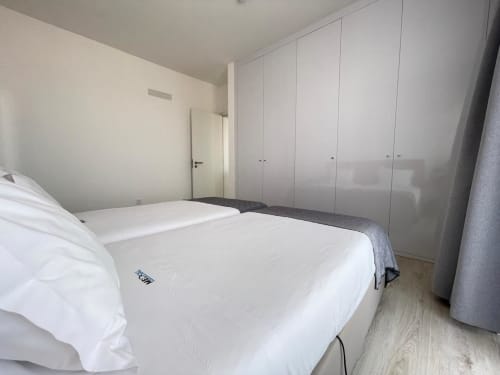 Quarto moderno no apartamento MedSal Residence Santa Maria com roupa de cama branca, guarda-roupas embutidos e vista da cidade