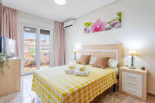 Dormitorio luminoso en apartamento Belchi Beach de San Pedro del Pinatar con ropa de cama amarilla estampada, muebles de madera y