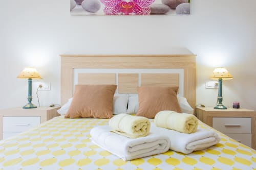 Dormitorio luminoso en apartamento de playa de Haus Holiday Homes en San Pedro del Pinatar con toallas enrolladas sobre ropa de cama amarilla con patrón.