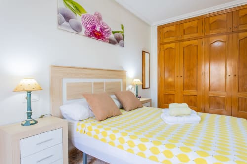 Luminosa habitación en Haus Holiday Homes San Pedro del Pinatar con ropa de cama amarilla estampada, armario de madera y orquídea