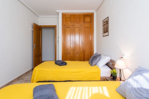Dormitorio luminoso en Haus Holiday Homes de San Pedro del Pinatar con dos camas individuales amarillas y armarios de madera