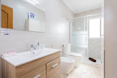 Baño moderno con mueble de madera, lavabo blanco, inodoro y ducha de cristal en Haus Holiday Homes en San Pedro del