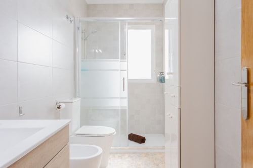 Baño moderno con ducha abierta, azulejos blancos, inodoro, bidé y tocador de madera en Haus Holiday Homes en San Pedro del