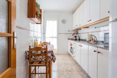 Cocina moderna tipo galera con mueblería blanca, detalles en madera y zona de comedor en apartamento Haus Holiday Homes, San Pedro del