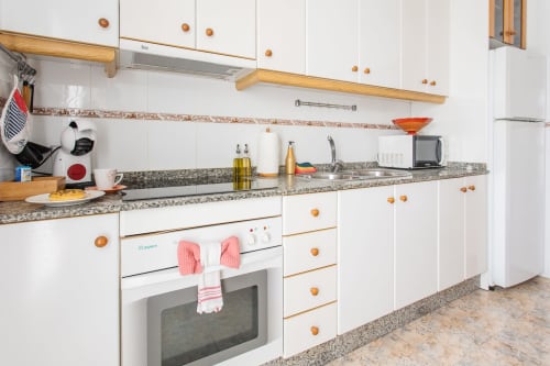 Cocina blanca moderna con tiradores de madera, encimera de granito y electrodomésticos de acero inoxidable en Haus Holiday Homes, San Pedro