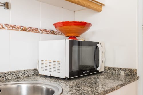 Encimera de cocina en Haus Holiday Homes San Pedro del Pinatar con microondas y cuenco decorativo rojo sobre el fregadero.