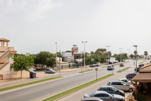 Vista de calle en San Pedro del Pinatar con el edificio de apartamentos Haus Holiday Homes, autos estacionados en un día soleado