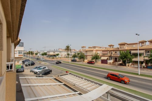 Apartamento en San Pedro del Pinatar con vista desde balcón a calle residencial, coches aparcados y edificios de terracota bajo cielo despejado