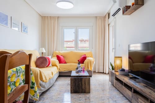 Luminosa sala de estar del apartamento Belchi Beach en San Pedro del Pinatar con sofá amarillo, cojines rojos, televisión y balcón