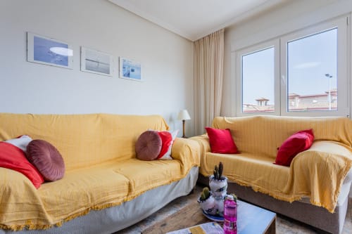 Luminosa sala de estar en Haus Holiday Homes en San Pedro del Pinatar con sofás amarillos, cojines rojos y ventanas con vista al mar.