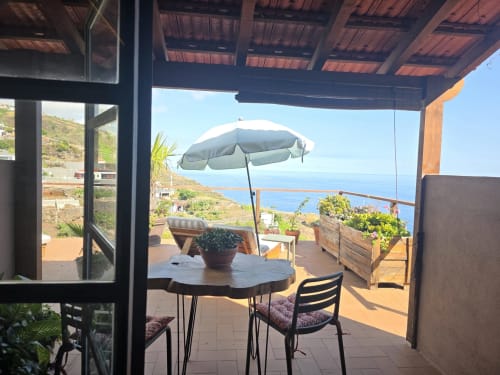 Terraza soleada con vista al mar en Les Terrasses Les Suites en Calheta, Portugal con mesa de comedor y sombrilla