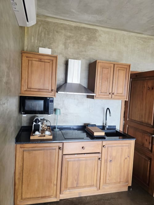 Cocineta con armarios de madera, encimera negra, estufa, microondas y cafetera en la Suite 3 de Les Terrasses Les