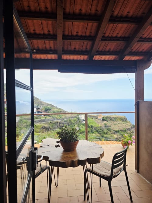 Terraza cubierta de Les Terrasses Les Suites con vistas al océano, mesa de madera, sillas y plantas en macetas con vista a Calheta