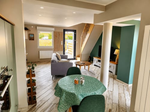 Moderne open leefruimte in Ô de Mer in Sangatte met groene accentwanden, rond eettafel, grijze fauteuil en trap