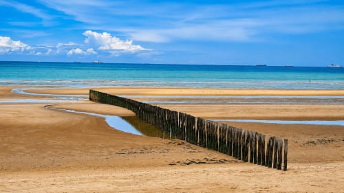 Sandy beach at Ô de Mer Sangatte with wooden breakwater, shallow pools, and turquoise sea under blue sky