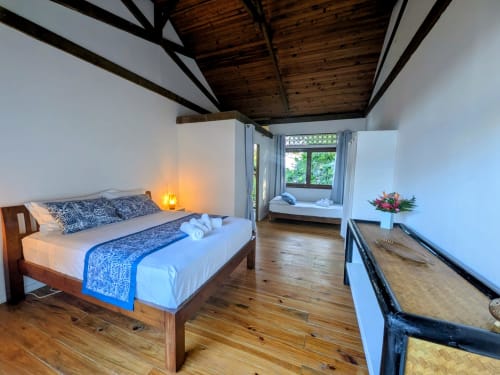 Chambre Faupapa au Fare Tihi Moana, Raiatea : poutres en bois, literie bleue et coin fenêtré