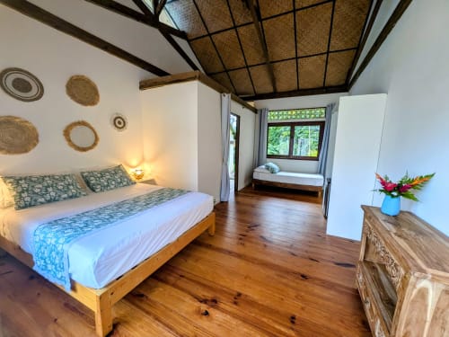 Chambre spacieuse à Fare Tihi Moana à Raiatea avec lit en bois, art mural tressé et vue sur le jardin