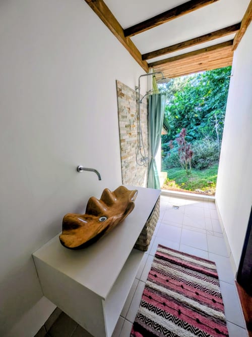 Salle de bains extérieure du Fare Tihi Moana avec lavabo en bois, mur de pierre et vue sur jardin luxuriant à Raiatea