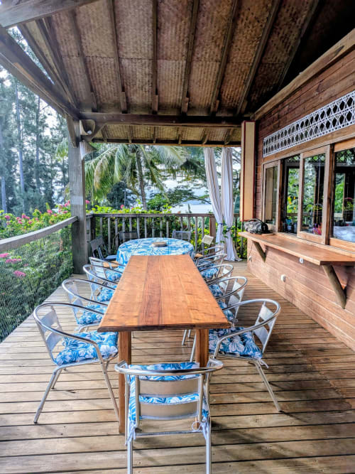 Terrasse couverte avec vue océan au Fare Tihi Moana, table à manger en bois et chaises bleues à motifs floraux à Raiatea