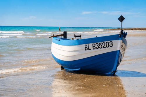Blue and white fishing boat on Sangatte beach near Ô de Mer hotel, clear sky and turquoise waters