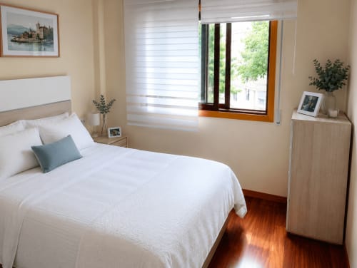 Dormitorio luminoso en el hotel Holibai de Baiona con cama blanca, suelo de madera y vistas al jardín