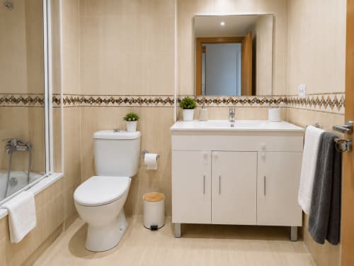 Baño moderno del hotel Holibai en Baiona con lavamanos blanco, inodoro y paredes de azulejos beige