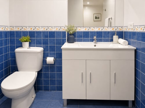Baño moderno en el hotel Holibai de Baiona con azulejos azules, lavabo blanco, inodoro y plantas decorativas