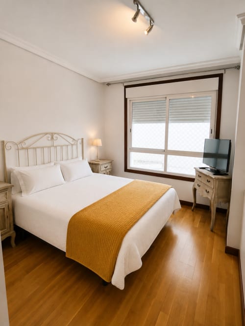 Habitación luminosa del hotel Holibai en Baiona con cama blanca, manta dorada, suelos de madera y ventanas con vistas al mar y persianas