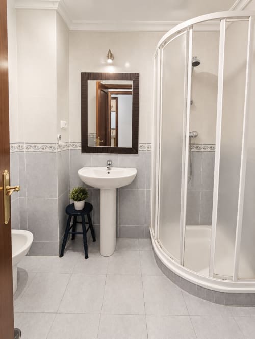 Baño moderno del hotel Holibai en Baiona con lavamanos pedestal, ducha curva y detalles decorativos de azulejos